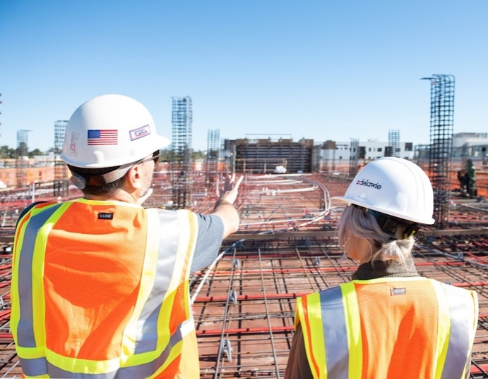 Two people in a white hardhat standing on the brown wooden dock during the daytime.