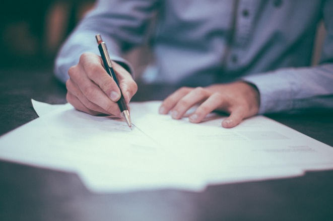 A person in a dress shirt signing a paper 