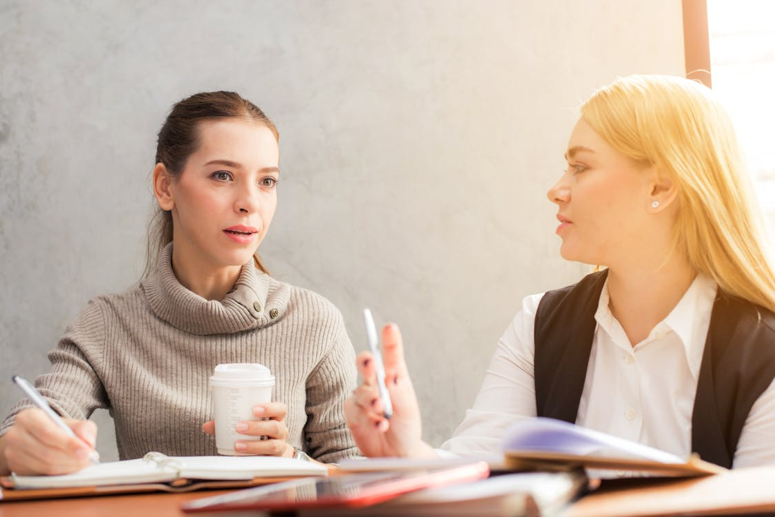 Two women talking to each other while holding a pen and making notes