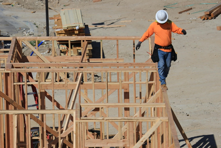 A construction worker walking next to an under-construction house 